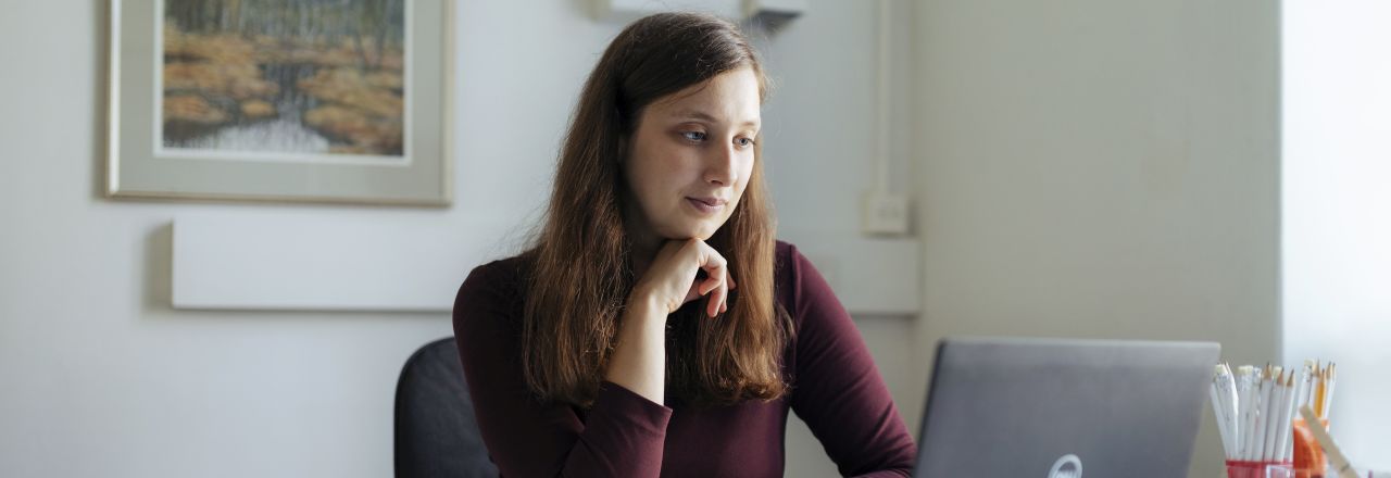 Ihminen istuu pöydän ääressä ja katselee tietokoneen näyttöä.