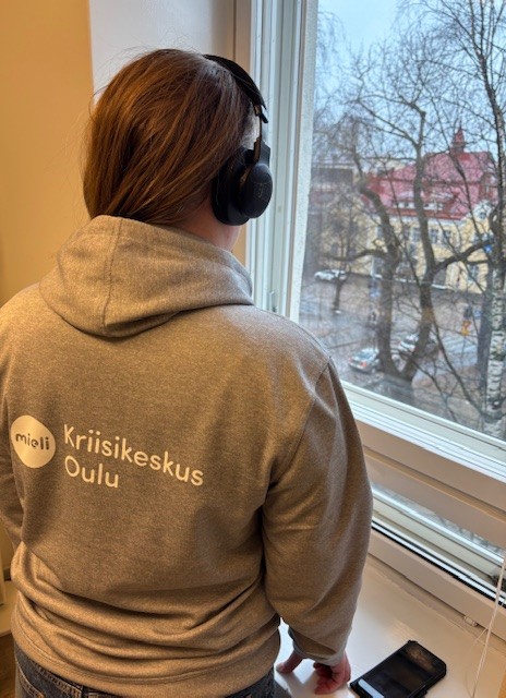 ihminen seisoo ikkunan edessä puhuen kuulokkeen päässä puhelimeen