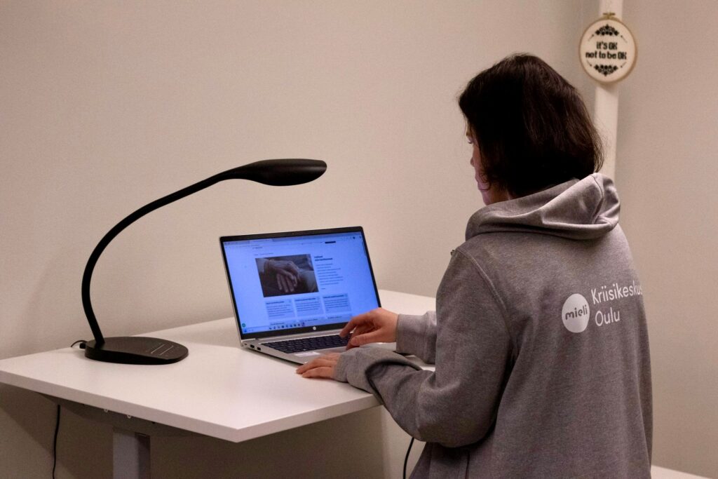 ihminen istuu tietokonepöydän äärellä ja käyttää konetta