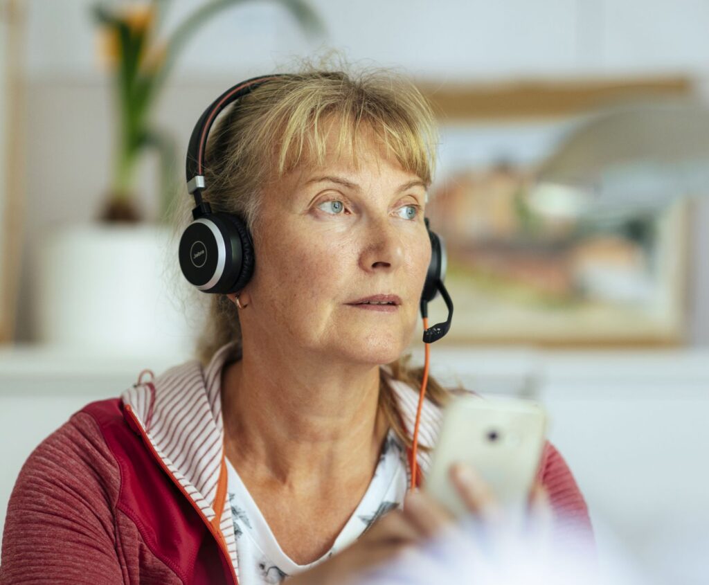 Nainen kuuntelee kuulokkeet korvillaan ja puhelin kädessään.