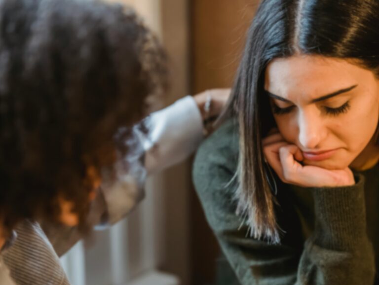 Kaksi nuorta lähikuvassa, toisen käsi surullisen henkilön olkapäällä
