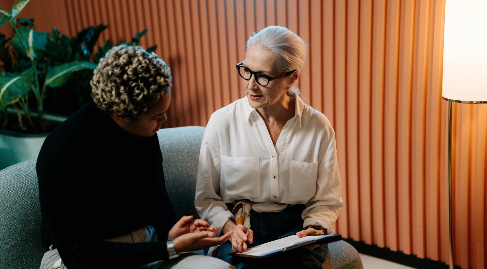 Kaksi naisoletettua istuu vierekkäin sohvalla ja keskustelee.